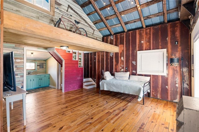 unfurnished bedroom with high vaulted ceiling, beamed ceiling, wooden walls, and hardwood / wood-style flooring