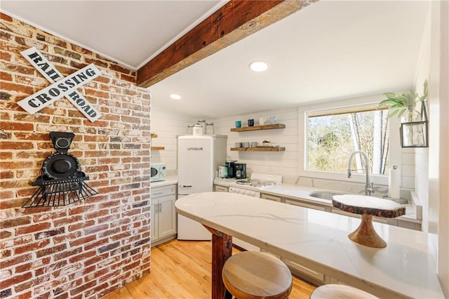 kitchen featuring white microwave, light wood-style flooring, light stone counters, beamed ceiling, and a sink