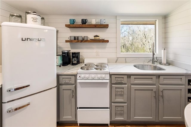 kitchen featuring light stone counters, open shelves, gray cabinets, a sink, and white appliances