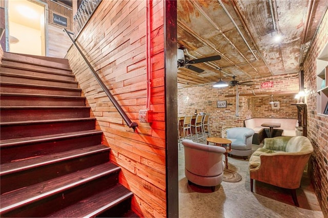 stairs with brick wall, ceiling fan, and concrete flooring