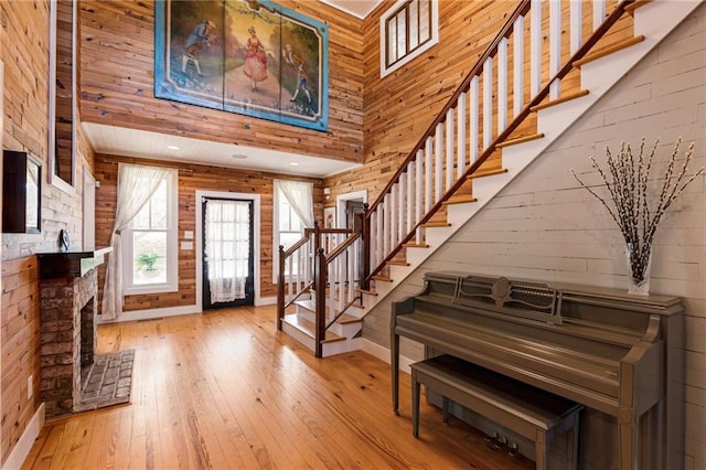 foyer entrance featuring a fireplace with raised hearth, wooden walls, a high ceiling, stairway, and hardwood / wood-style floors