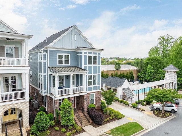 view of front of house featuring central AC, brick siding, board and batten siding, a balcony, and a standing seam roof