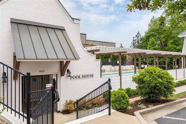 property entrance featuring fence, a community pool, a pergola, and brick siding