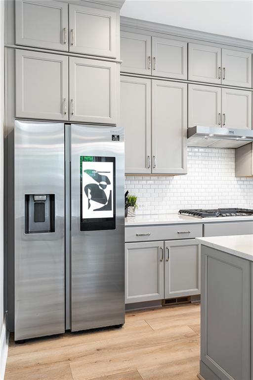 kitchen featuring under cabinet range hood, stainless steel refrigerator with ice dispenser, gray cabinetry, and gas cooktop