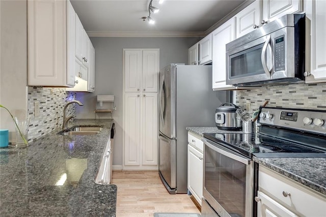 kitchen featuring appliances with stainless steel finishes, a sink, light wood-style floors, white cabinetry, and ornamental molding