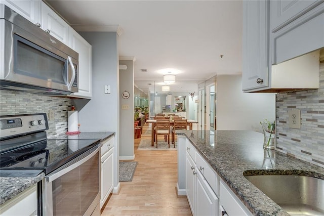 kitchen with stainless steel appliances, crown molding, light wood finished floors, decorative backsplash, and white cabinetry