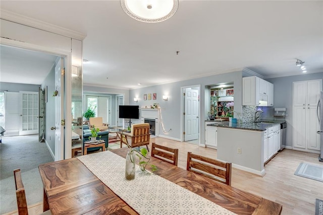 dining room featuring ornamental molding, baseboards, a fireplace, and light wood-style floors