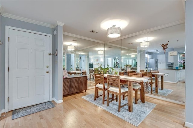 dining area with light wood-style floors, crown molding, and baseboards