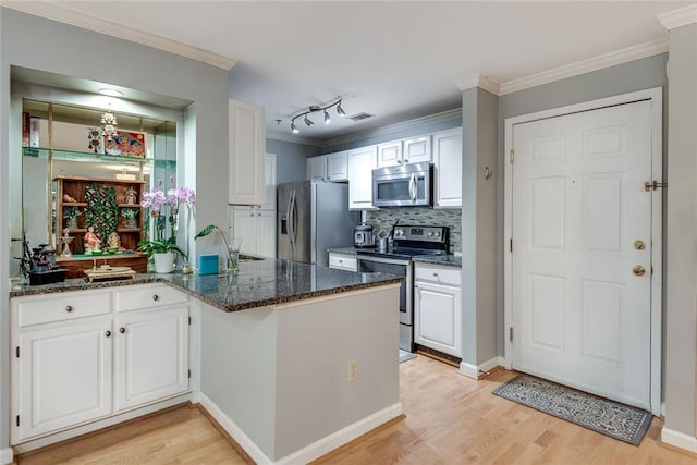 kitchen with appliances with stainless steel finishes, light wood-type flooring, white cabinetry, dark stone countertops, and backsplash