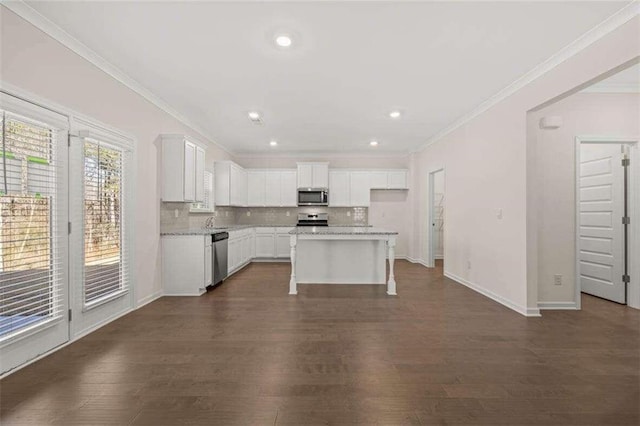 kitchen featuring appliances with stainless steel finishes, white cabinetry, tasteful backsplash, ornamental molding, and a kitchen island