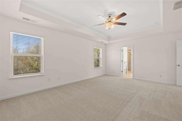 empty room featuring ceiling fan, light colored carpet, and a tray ceiling