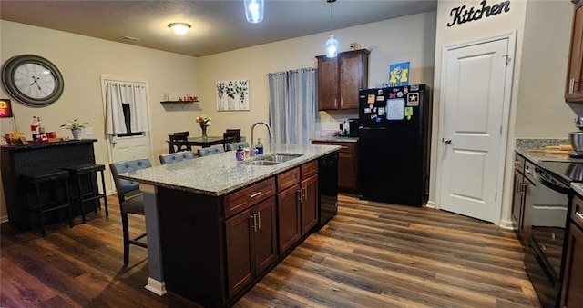 kitchen with dark wood-type flooring, sink, hanging light fixtures, a kitchen island with sink, and black appliances