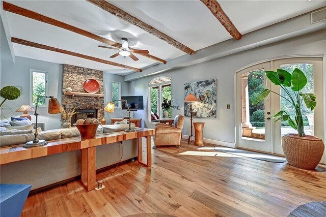 living room featuring light hardwood / wood-style floors, a stone fireplace, plenty of natural light, and ceiling fan