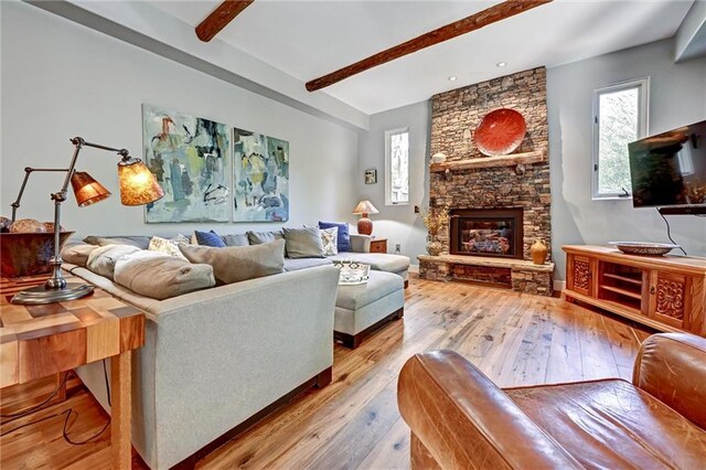 living room with a stone fireplace, light hardwood / wood-style flooring, and beam ceiling