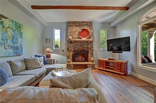 living room featuring a stone fireplace, beamed ceiling, and light wood-type flooring