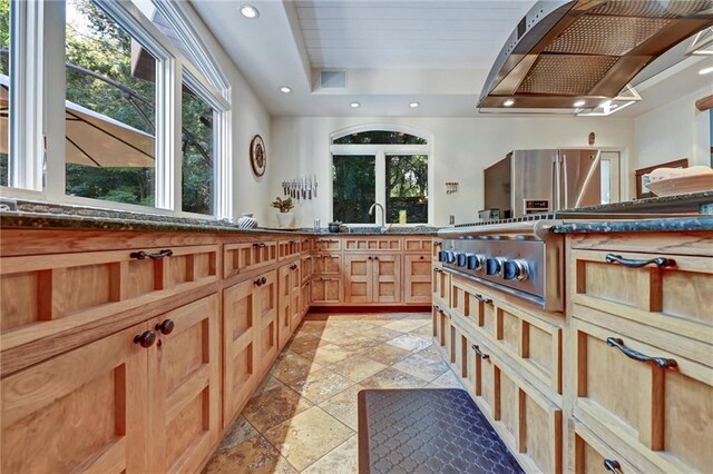 kitchen with a raised ceiling, stainless steel refrigerator, and exhaust hood