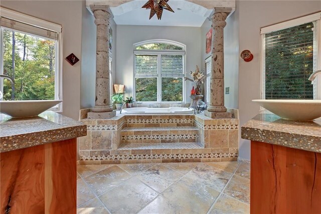 bathroom with sink, ornate columns, and tiled bath