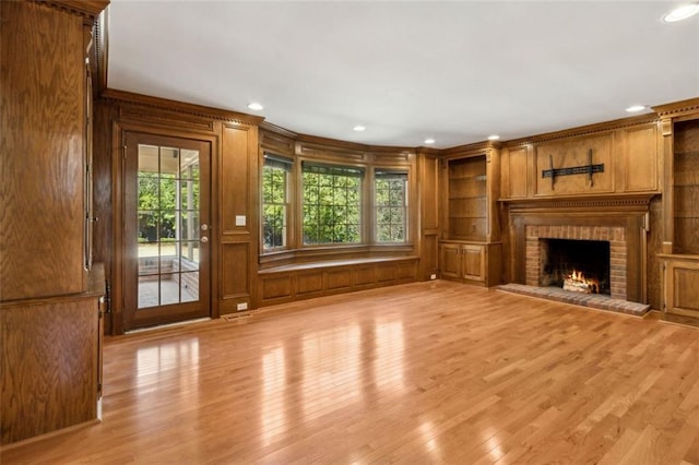 unfurnished living room with a wealth of natural light, wood walls, built in shelves, and light wood-type flooring