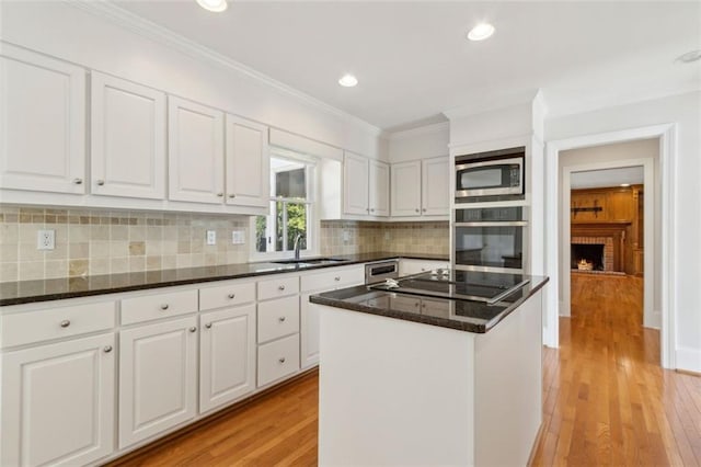 kitchen featuring light wood-style flooring, a sink, ornamental molding, stainless steel appliances, and white cabinets