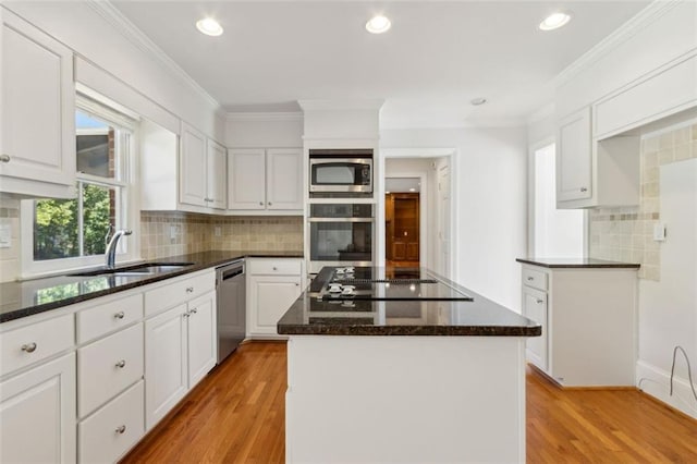 kitchen with dark stone counters, light wood-style flooring, appliances with stainless steel finishes, white cabinetry, and a sink