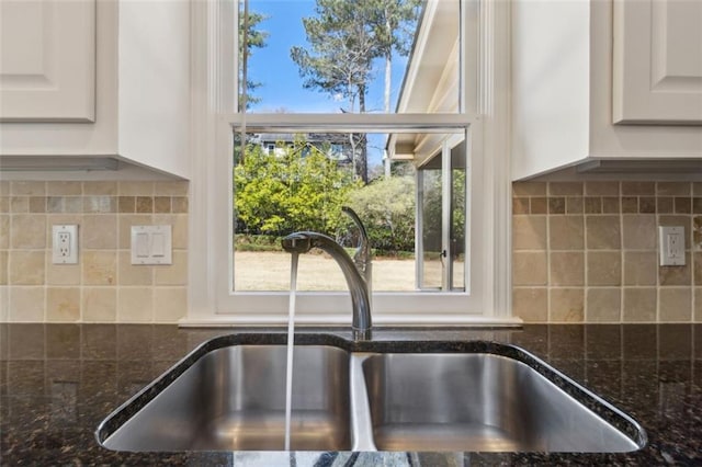 room details featuring tasteful backsplash, white cabinetry, dark stone counters, and a sink