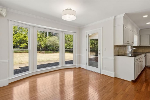 kitchen with a sink, dark countertops, tasteful backsplash, wood-type flooring, and crown molding