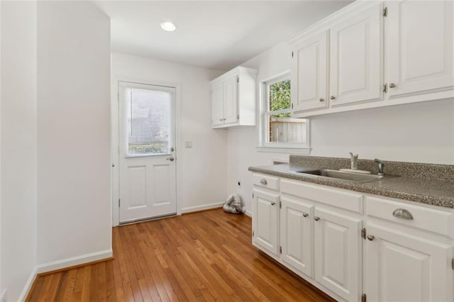 laundry area with baseboards, light wood-style floors, cabinet space, hookup for an electric dryer, and a sink