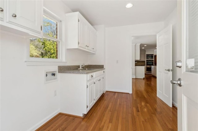 clothes washing area featuring wood finished floors, baseboards, cabinet space, a sink, and washer hookup