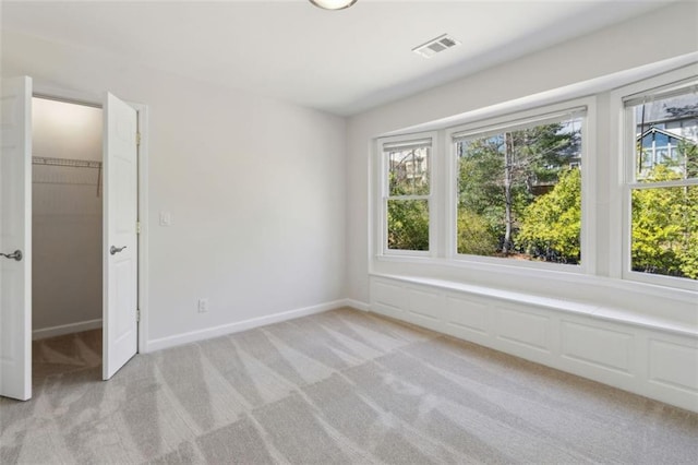 unfurnished room with a wealth of natural light, visible vents, light colored carpet, and baseboards