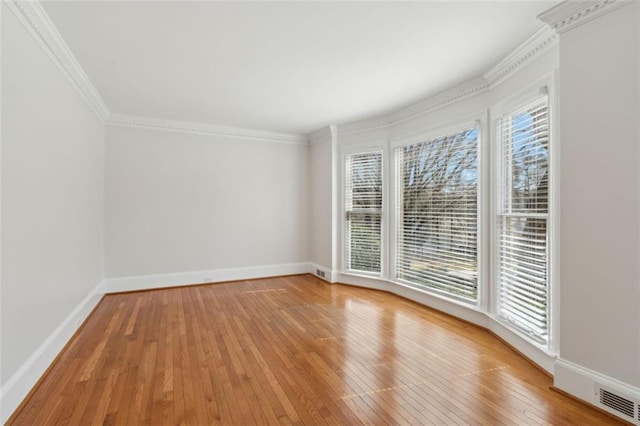 empty room featuring crown molding, light wood-type flooring, and baseboards