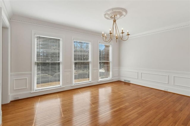 empty room with visible vents, light wood-style floors, a chandelier, and crown molding