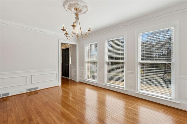 unfurnished room featuring visible vents, wood-type flooring, a chandelier, and ornamental molding