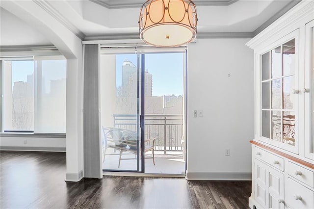 interior space with a raised ceiling, dark wood finished floors, arched walkways, crown molding, and baseboards