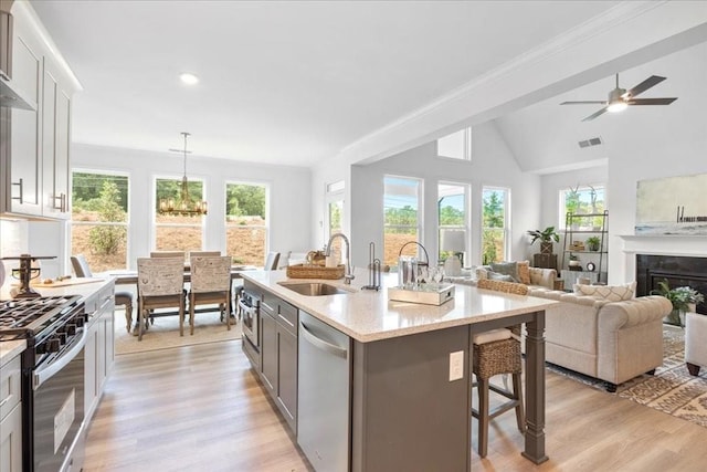 kitchen featuring a center island with sink, sink, stainless steel appliances, hanging light fixtures, and a breakfast bar area