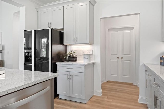 kitchen featuring backsplash, light hardwood / wood-style floors, light stone counters, and black fridge