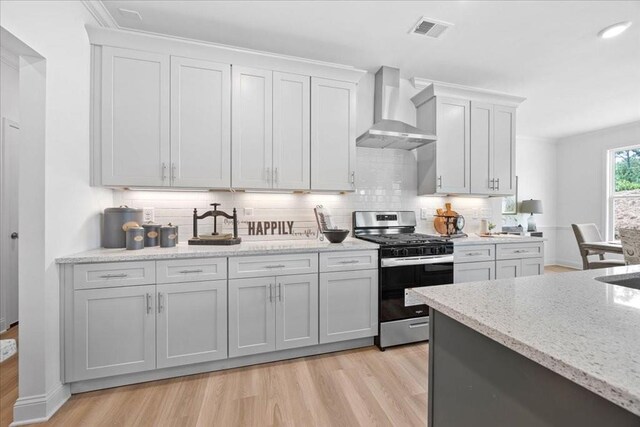 kitchen featuring tasteful backsplash, wall chimney exhaust hood, light stone countertops, light hardwood / wood-style floors, and stainless steel gas stove