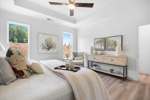 bedroom featuring a tray ceiling, ornamental molding, ceiling fan, and light hardwood / wood-style flooring