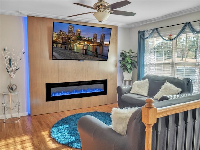 living area with ceiling fan, wood finished floors, baseboards, ornamental molding, and a glass covered fireplace