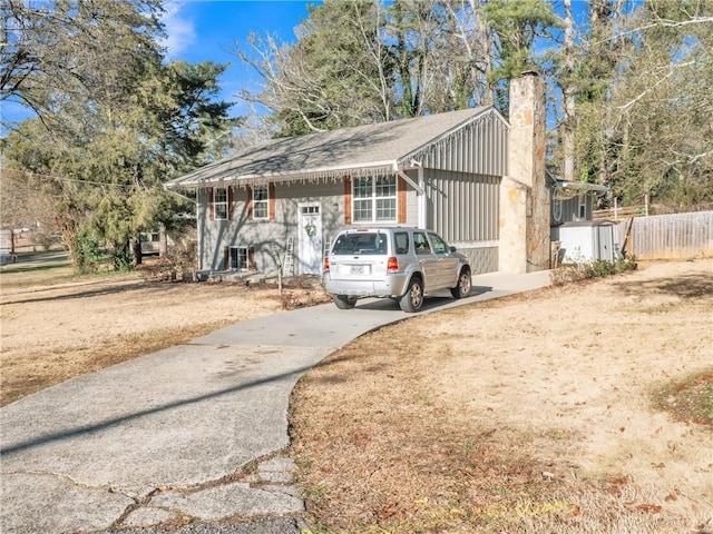 view of front of home with driveway, a chimney, and fence