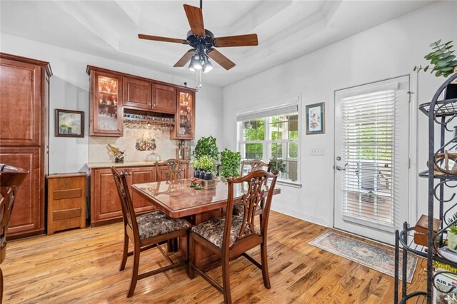 dining room featuring a raised ceiling, light wood-type flooring, and ceiling fan