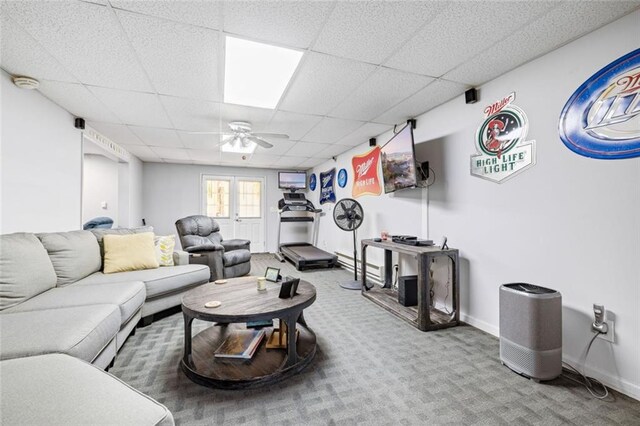 living area with a ceiling fan, a drop ceiling, carpet, and baseboards