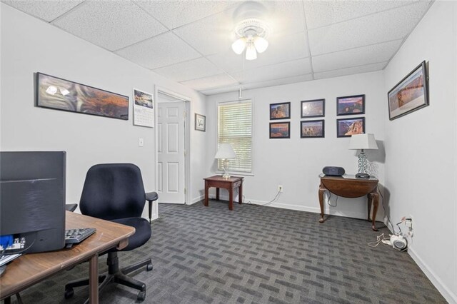 carpeted office with a drop ceiling, baseboards, and ceiling fan