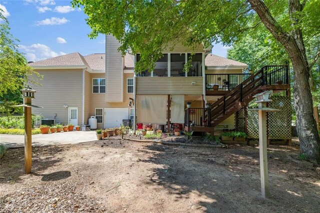 rear view of house with stairway, a sunroom, a patio area, a wooden deck, and driveway