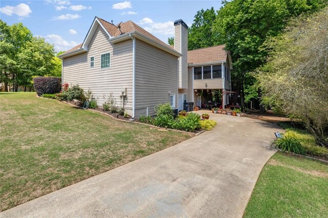 view of property exterior with concrete driveway, a yard, a chimney, and a sunroom