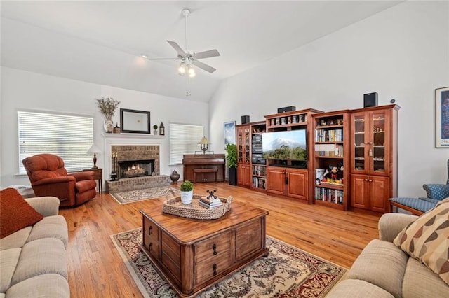 living room with light wood-style floors, a ceiling fan, high vaulted ceiling, plenty of natural light, and a fireplace