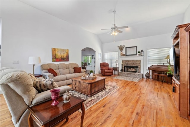 living area with a ceiling fan, arched walkways, a fireplace, light wood-type flooring, and lofted ceiling