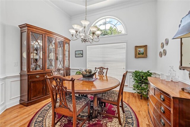dining area with a chandelier, light wood-style floors, wainscoting, a decorative wall, and crown molding