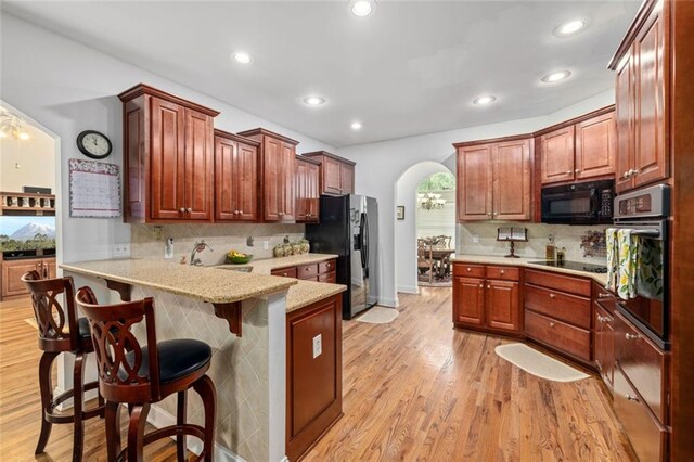 kitchen with black appliances, arched walkways, tasteful backsplash, a peninsula, and recessed lighting