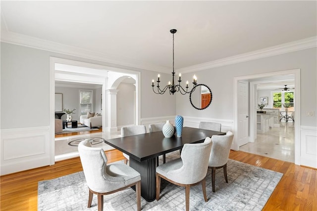 130 Robin Rd, Marietta, GA 30067 - dining room featuring arched walkways, a chandelier, ornamental molding, light wood-type flooring, and a wainscoted wall