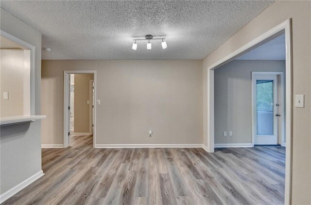 unfurnished room with baseboards, wood finished floors, and a textured ceiling